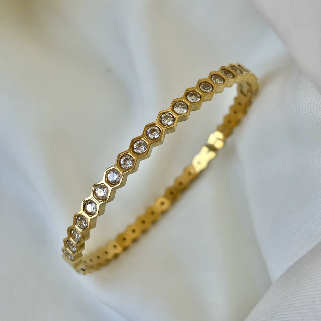 18K Gold plated bangle with glass crystal stones on a soft white fabric background.