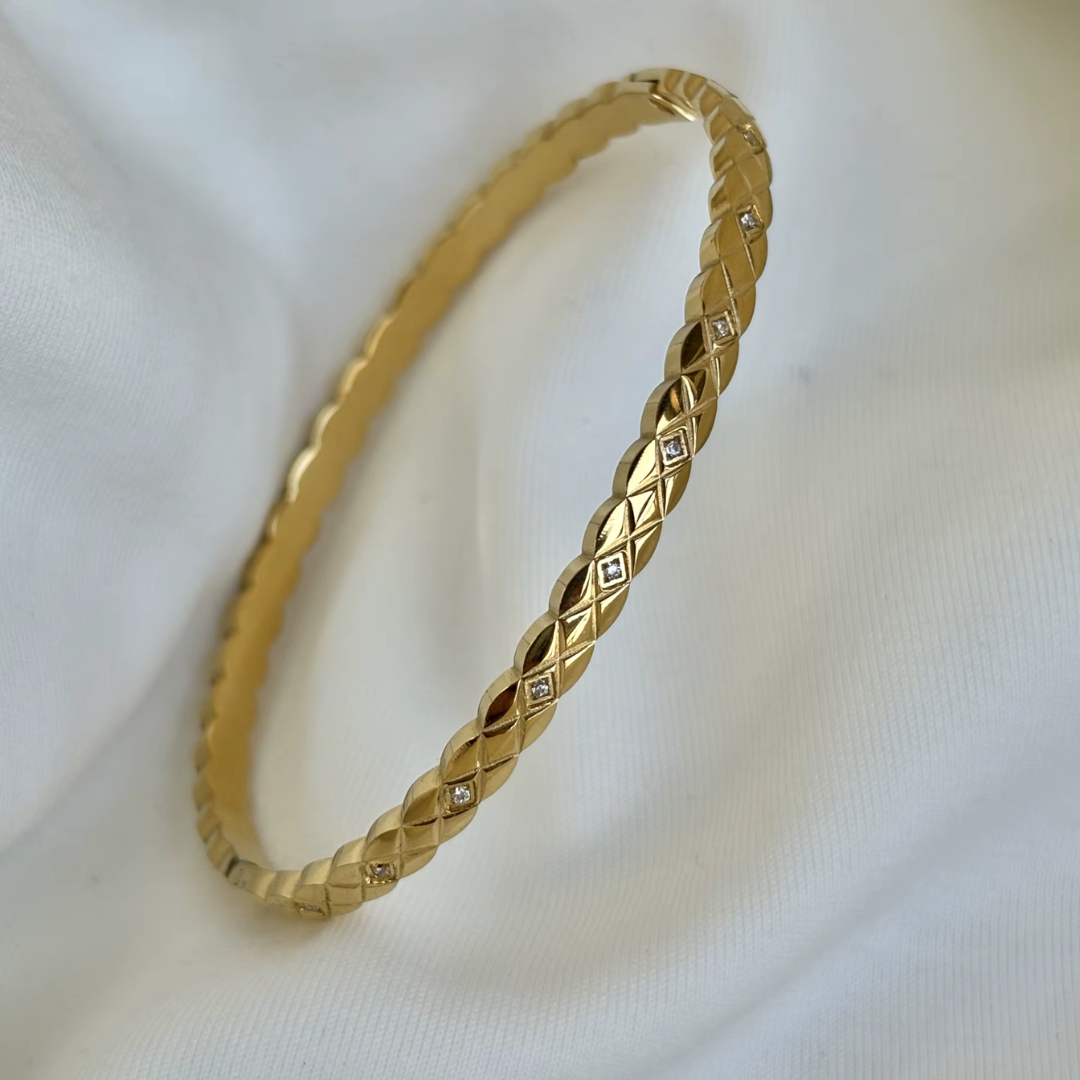 18K Gold plated non tarnish bangle with glass crystal stones on a white fabric background.