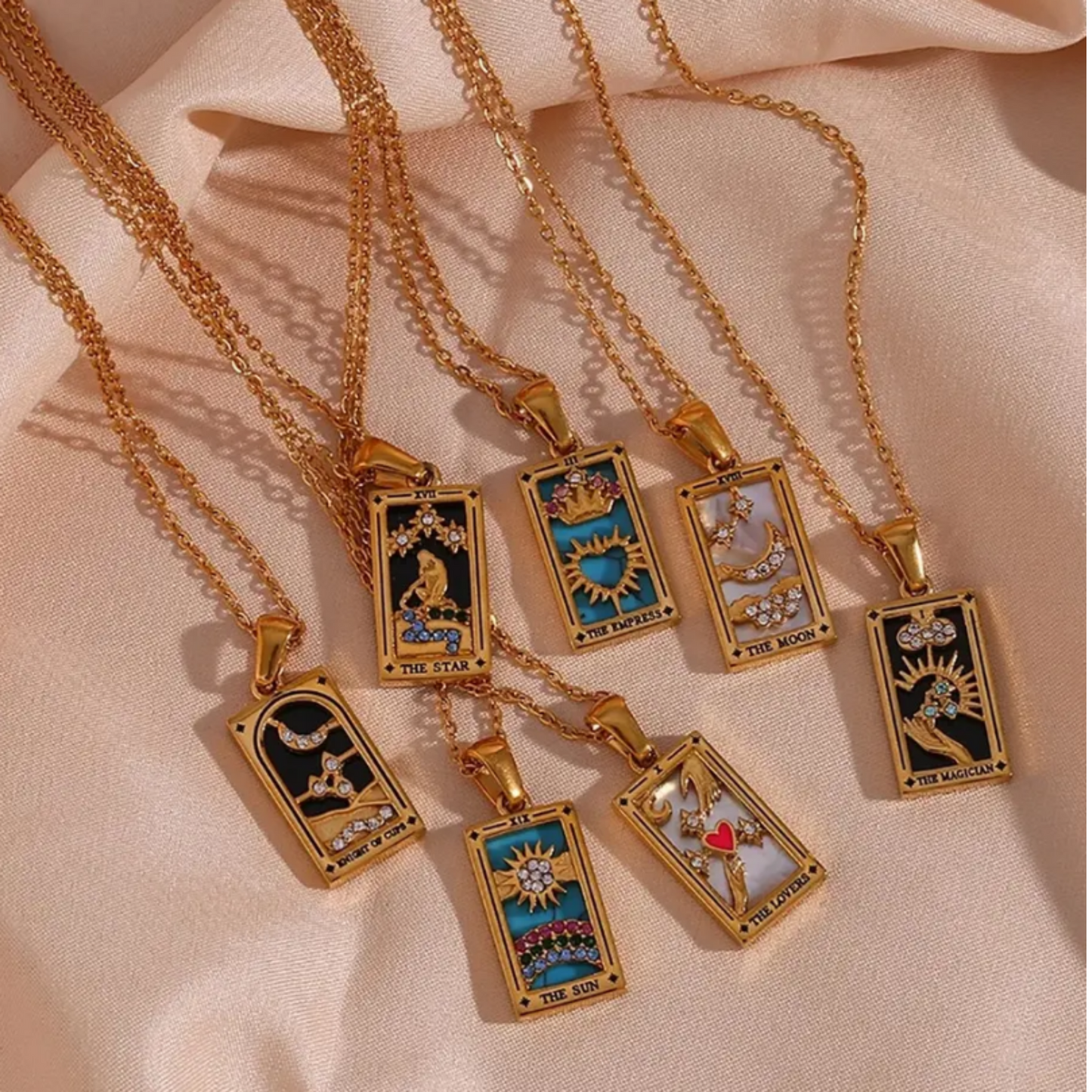 18K gold plated tarot card necklaces with a pendants and a chain extension laid on a nude fabric background.