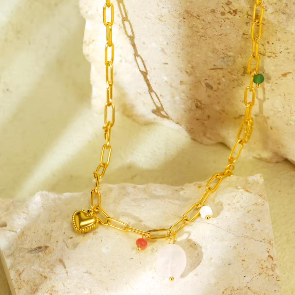 A 18K Gold Plated Rose Quartz Charm Necklace in the sun on a stone Slab.