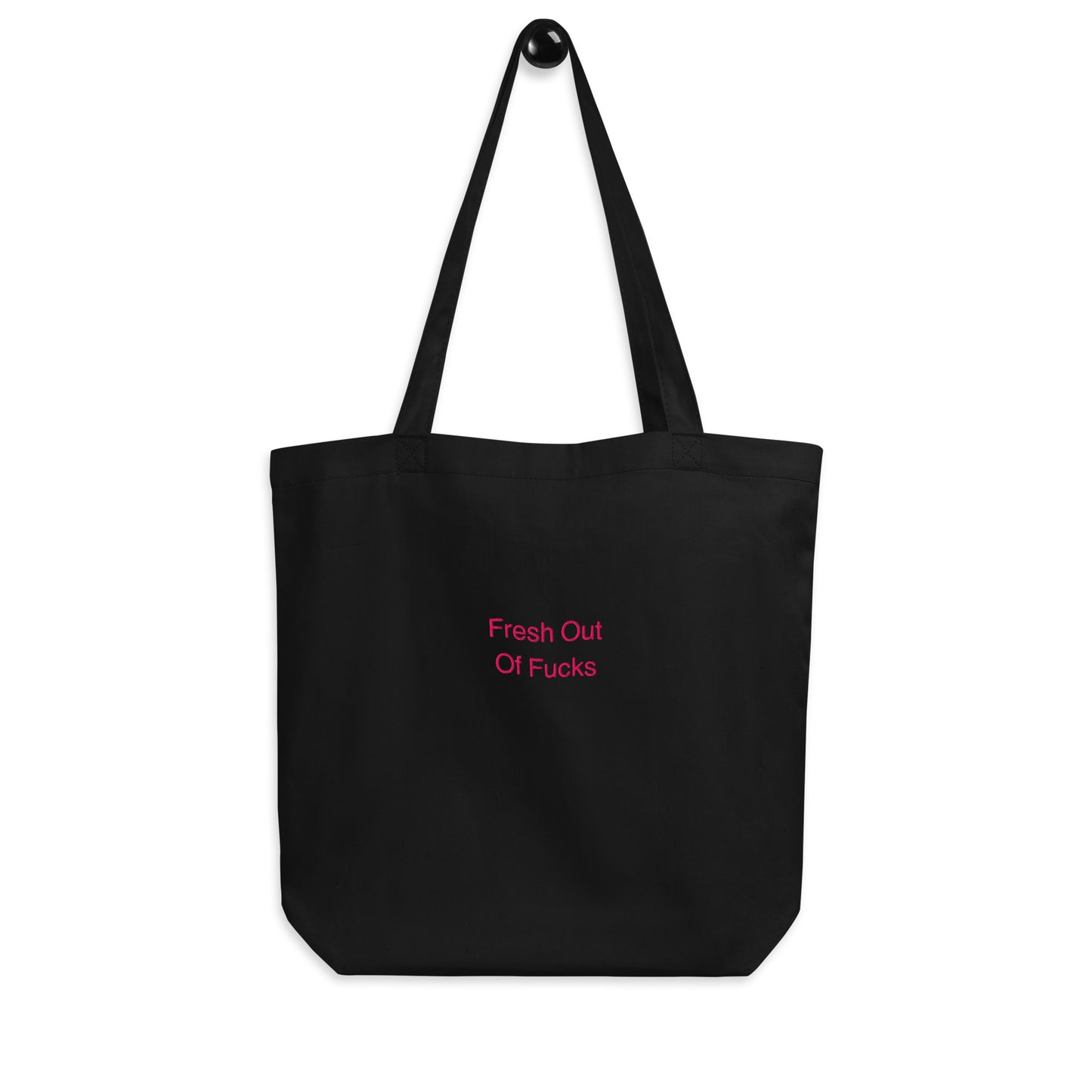 Black Fresh Out Of Fucks organic cotton Slogan embroidered eco tote bag on a blank surface hanging on a hook.