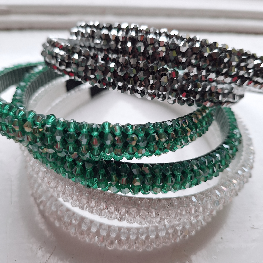 Three sparkle rhinestone headbands in charcoal grey, emerald green and clear beads on a white surface.