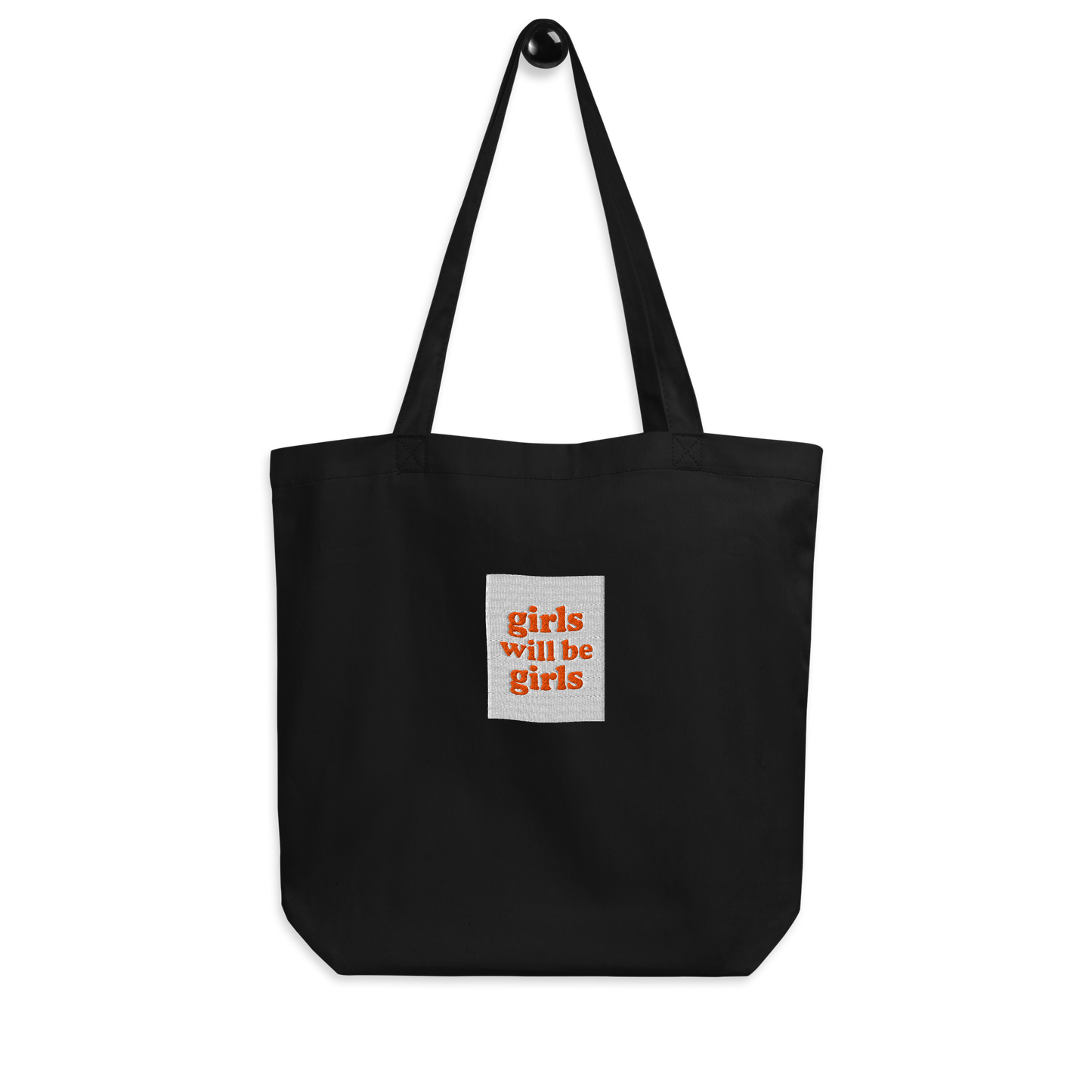 Black tote bag with a small embroidered square patch with the words girls will be girls on a white background.