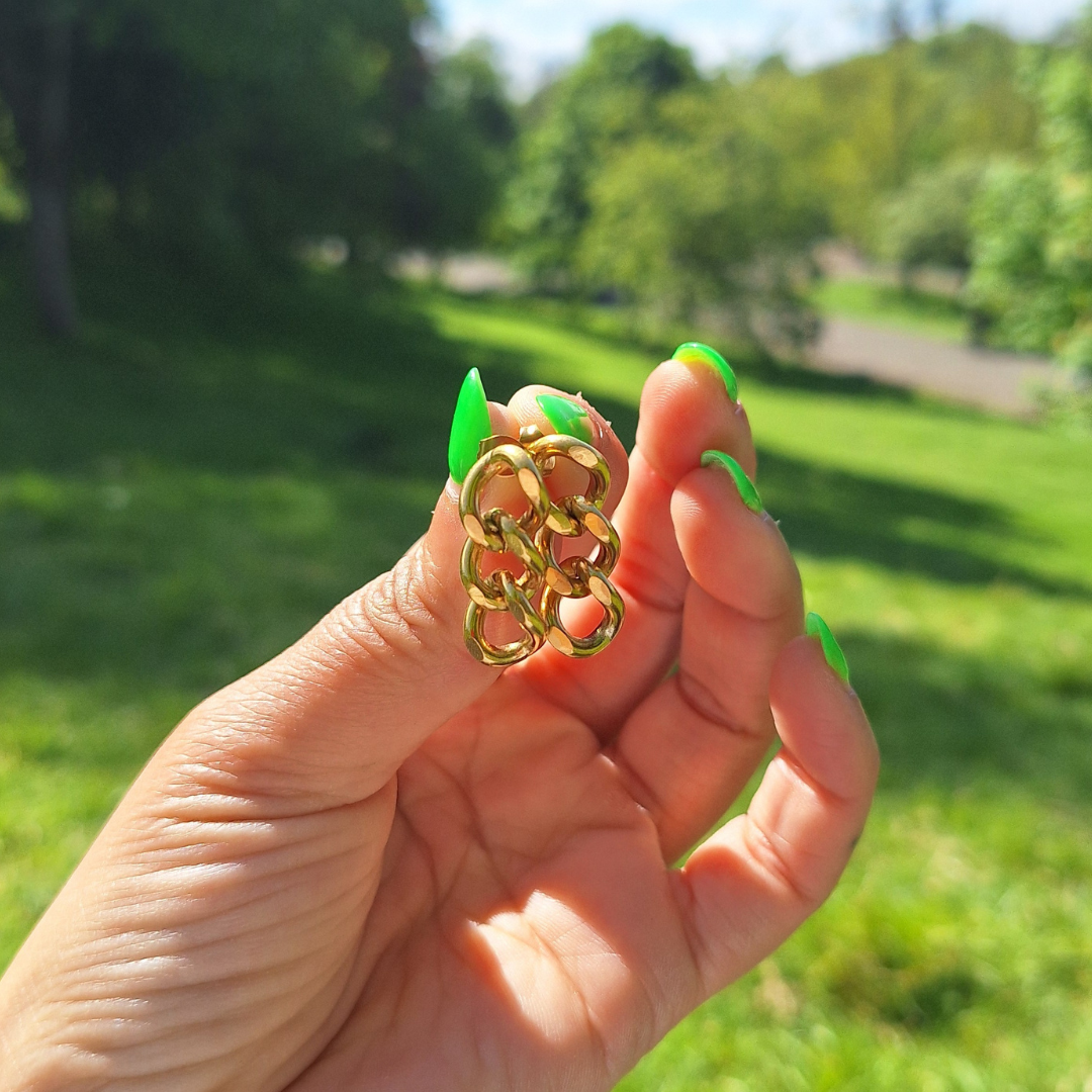 A hand holding stainless steel gold plated curb chain earrings in a park.