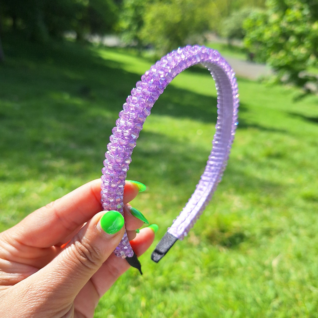 Bright lilac rhinestone summer headband being held by a hand in a park in the sun.