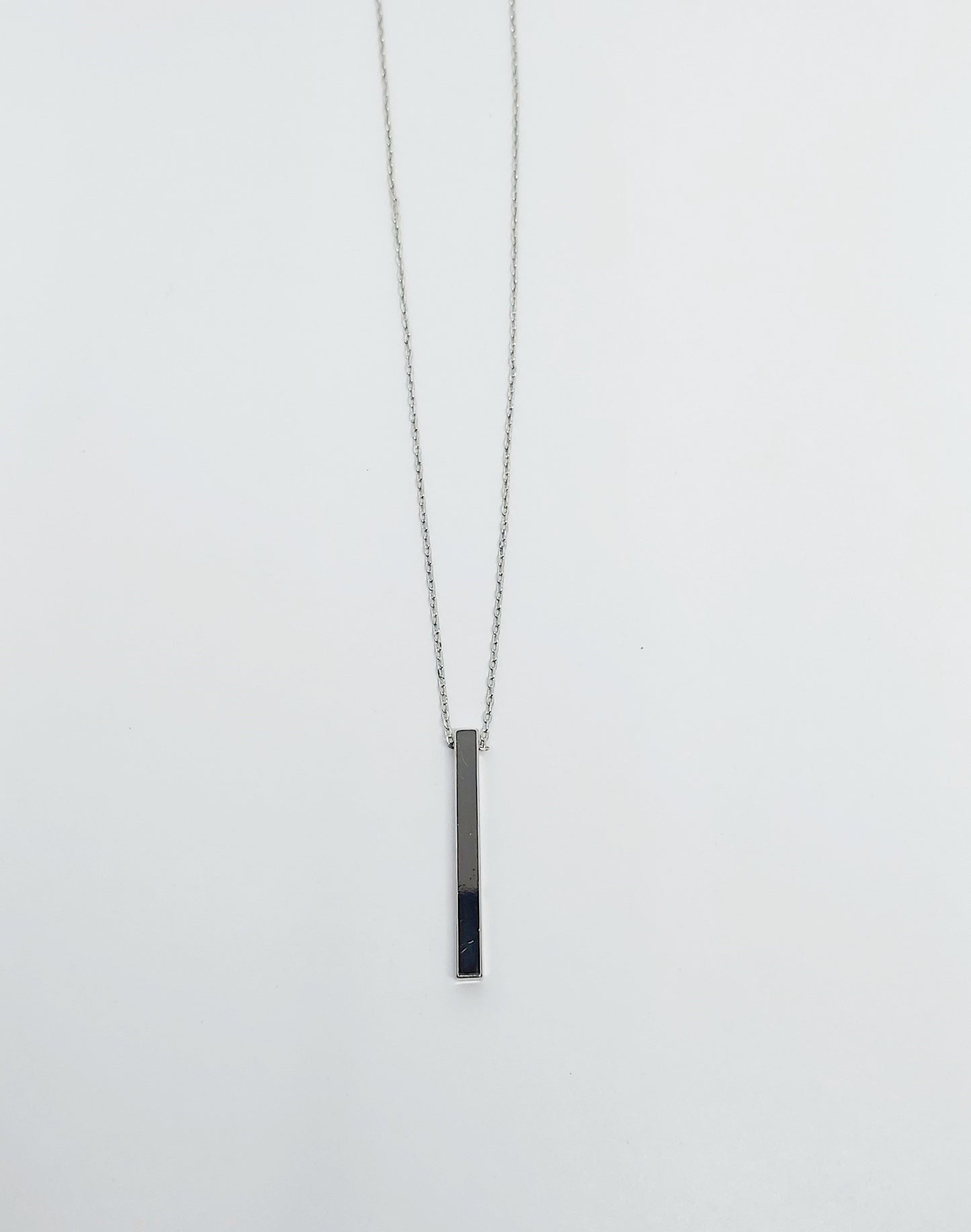 A silver-plated brass necklace with a geometric pendant in the shape of a circle and a bar, displayed on a white background.
