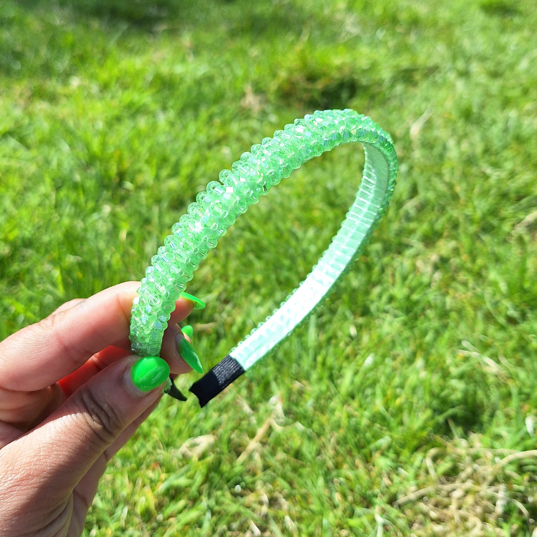 Bright mint rhinestone summer headband being held by a hand in a park in the sun.