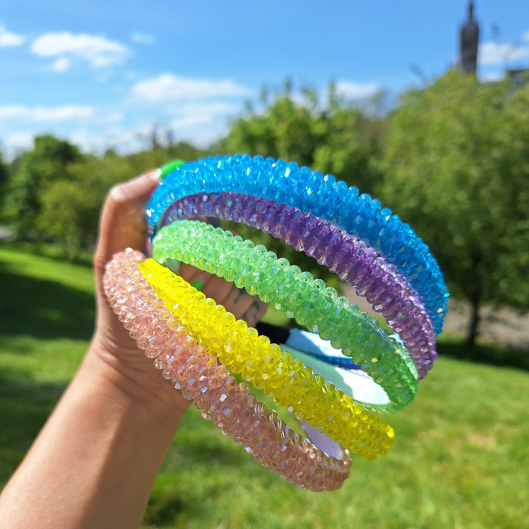 Bright rhinestone summer headbands in various colours being held by a hand in a park in the sun.