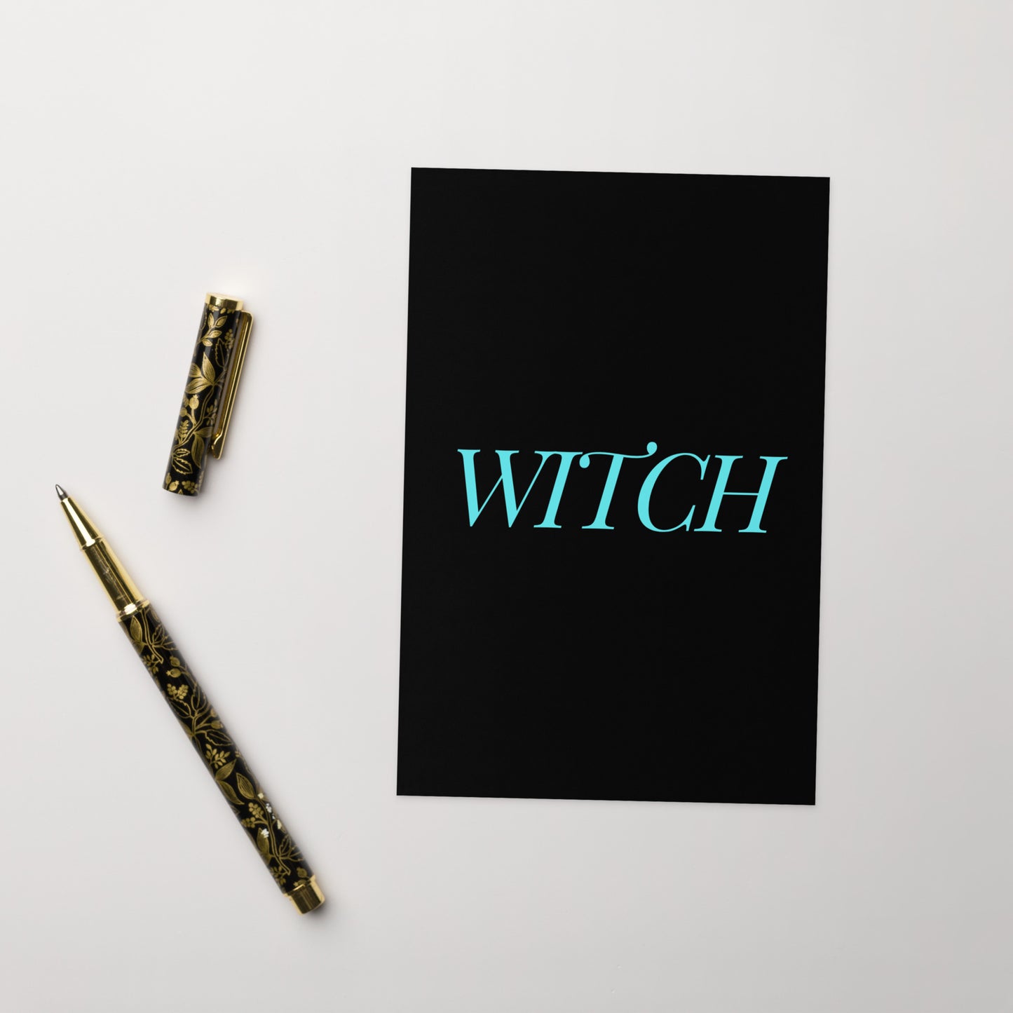 A funny witch greeting card on a white surface with a vintage fountain pen at the side.