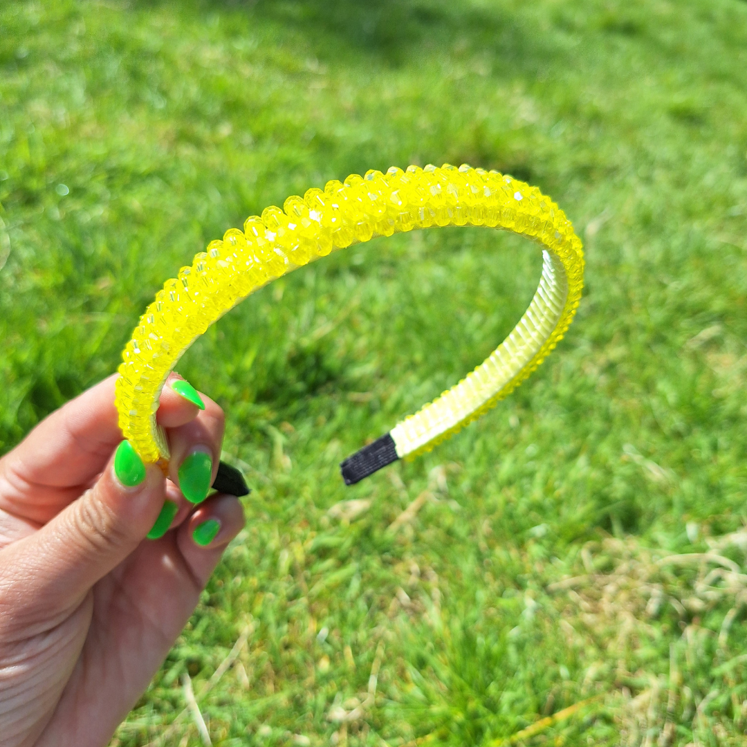 Bright yellow rhinestone summer headband being held by a hand in a park in the sun.