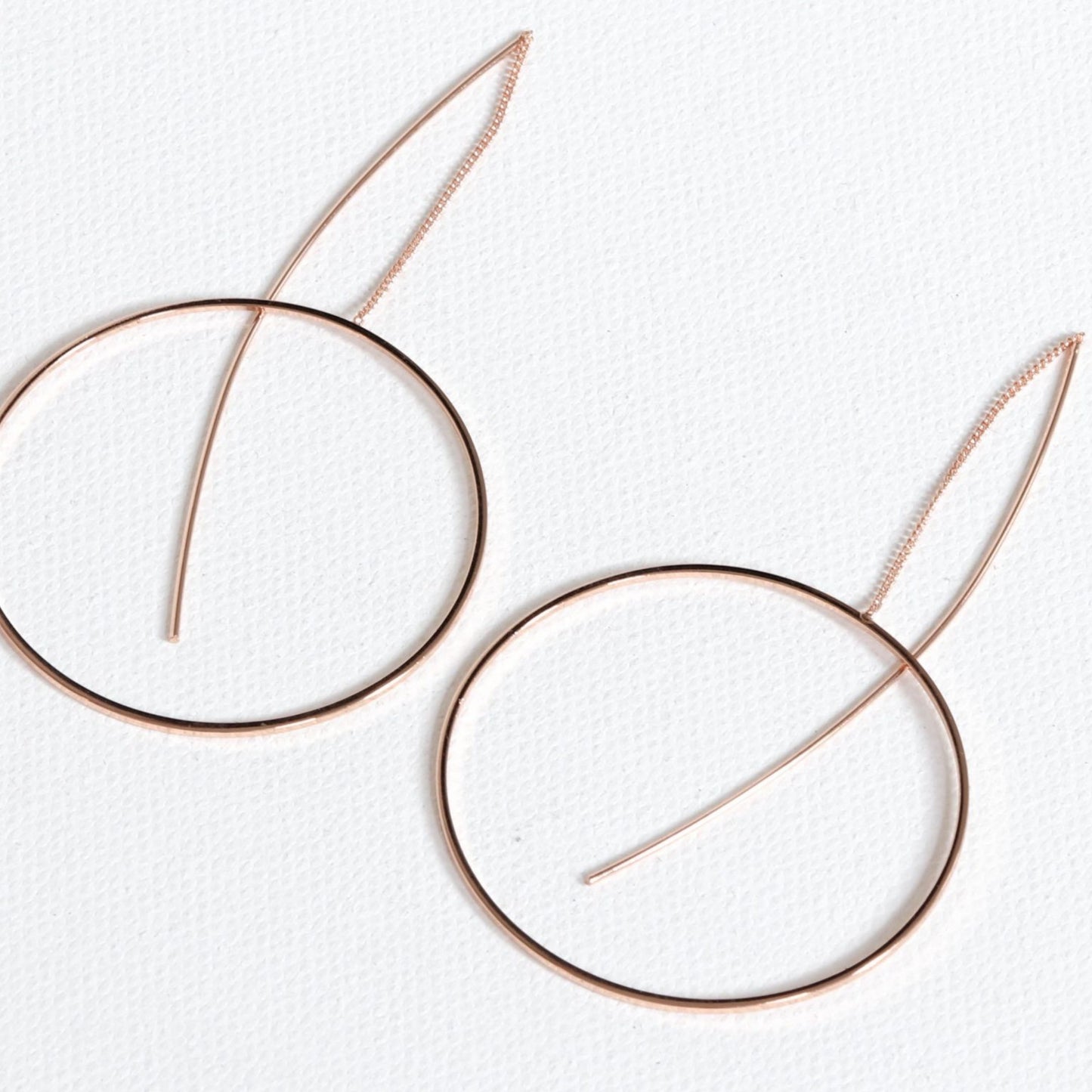 A pair of gold-plated circle pull-through earrings on a white background, showcasing the earrings' full length and circular design.