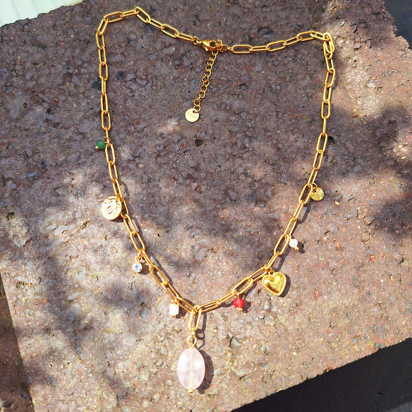 A 18K Gold Plated Rose Quartz Charm Necklace in the sun on a stone Slab.