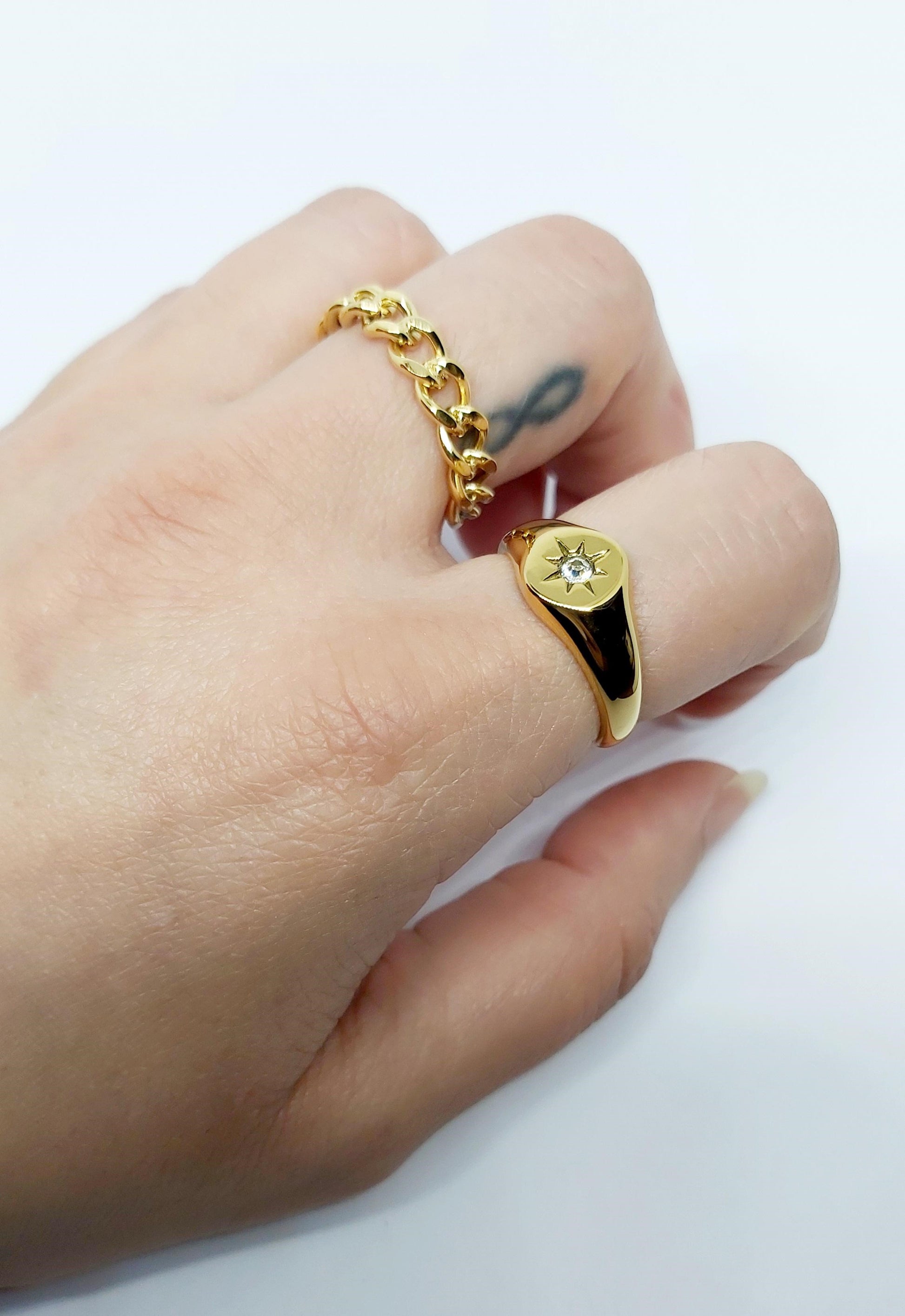18K Gold Plated Sparkle Signet Ring and gold curb chain ring on a a hand on a white background.