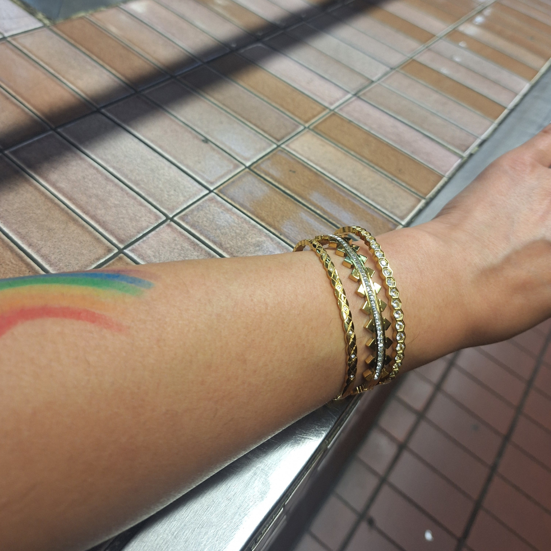 Close-up of a wrist wearing 18K gold plated tarnish free bangles on a blurred background.