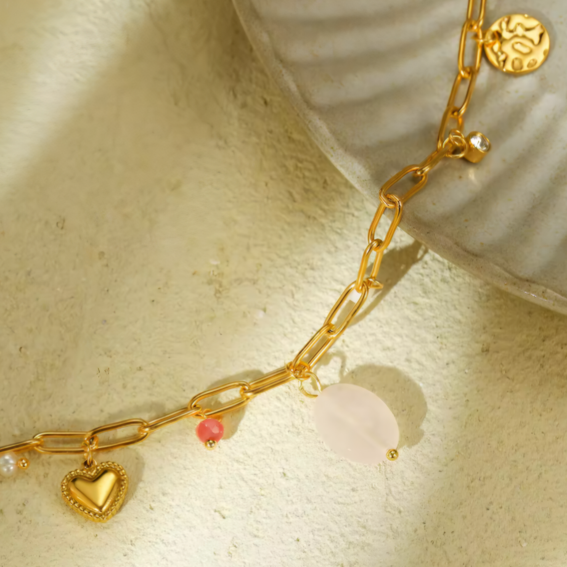 A 18K Gold Plated Rose Quartz Charm Necklace in the sun on a stone Slab.