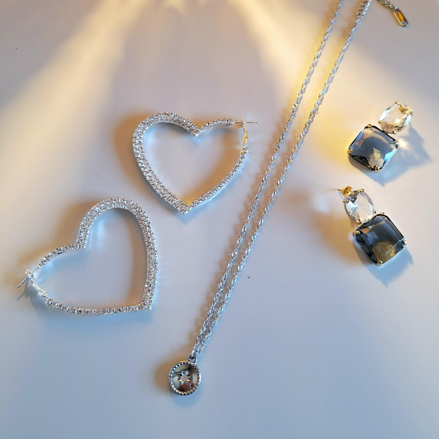 A pair of upcycled gold plated blue lux drop earrings, a circle and crystal pendant and sparkle heart hoops on a white background.