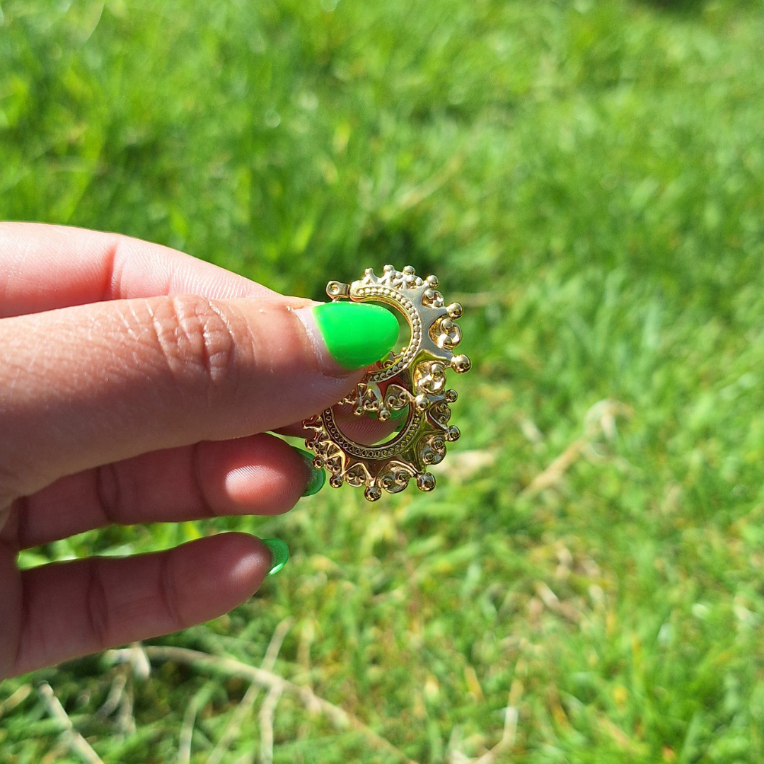 A hand with neon green nails holding a pair of gold plaited Arabian creole hoops in the sun.