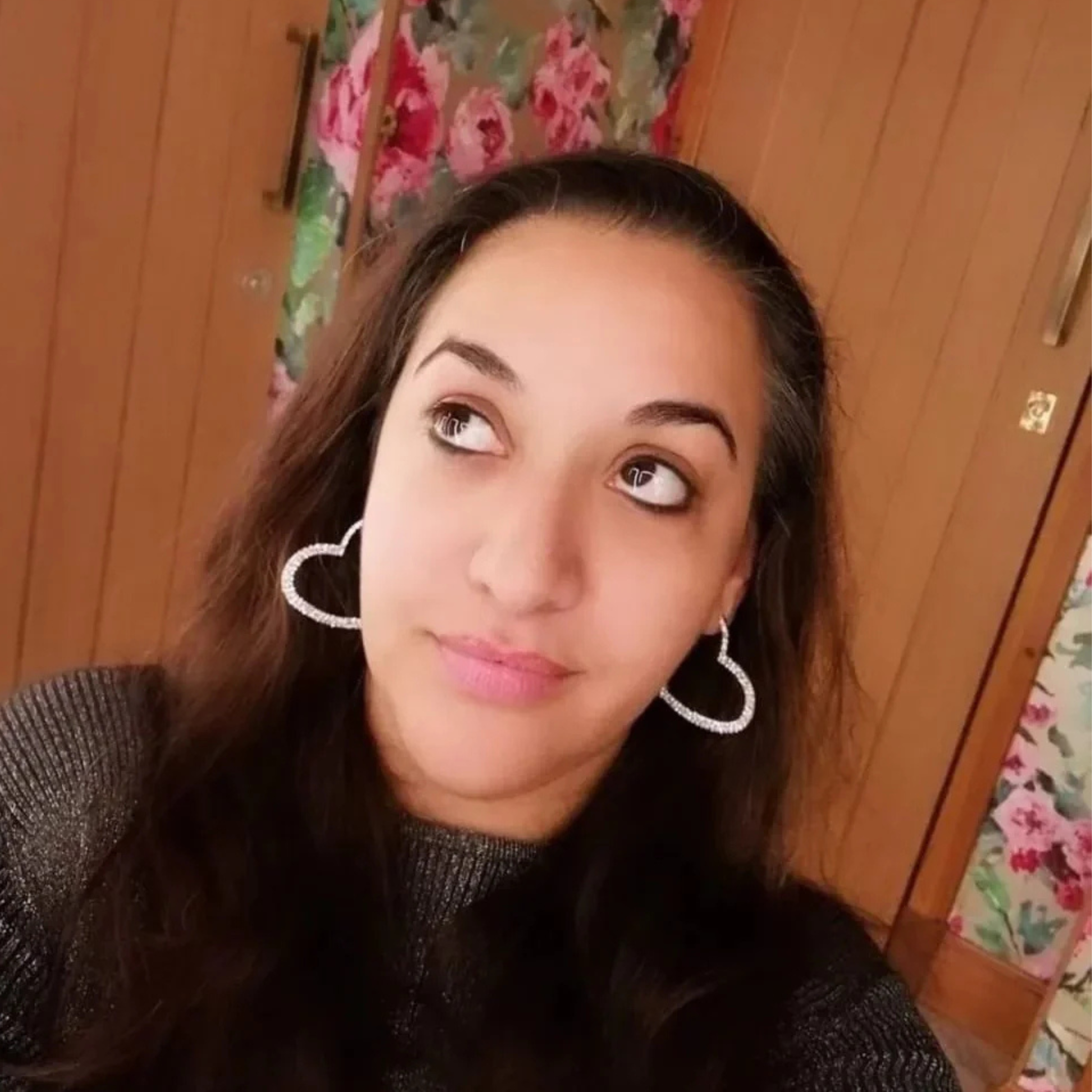 Woman wearing stainless steel sparkle heart-shaped earrings in a room with wooden walls and floral decorations.