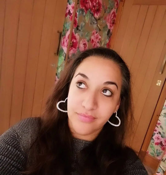 A person wearing the silver sparkle heart hoop earrings with a floral background.