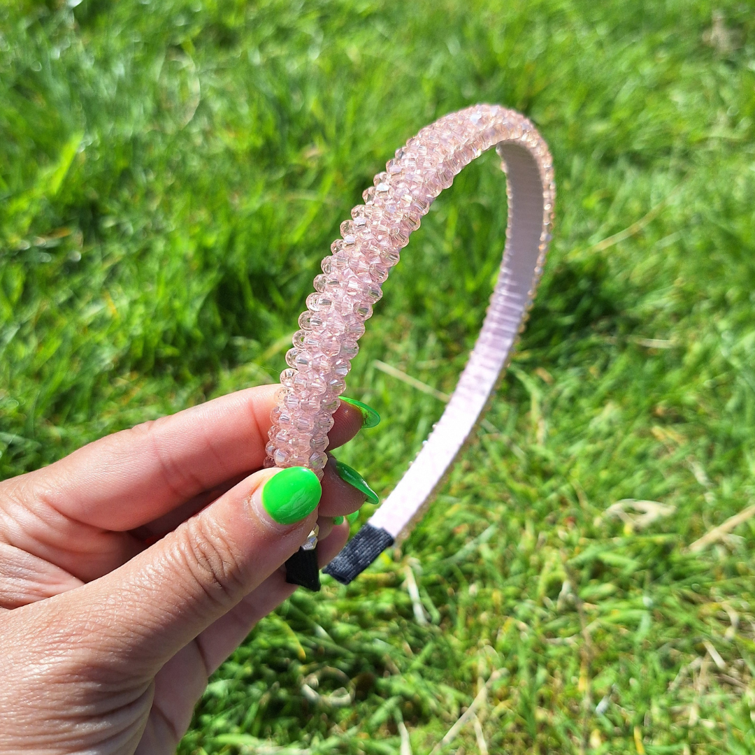 Bright blush rhinestone summer headband being held by a hand in a park in the sun.