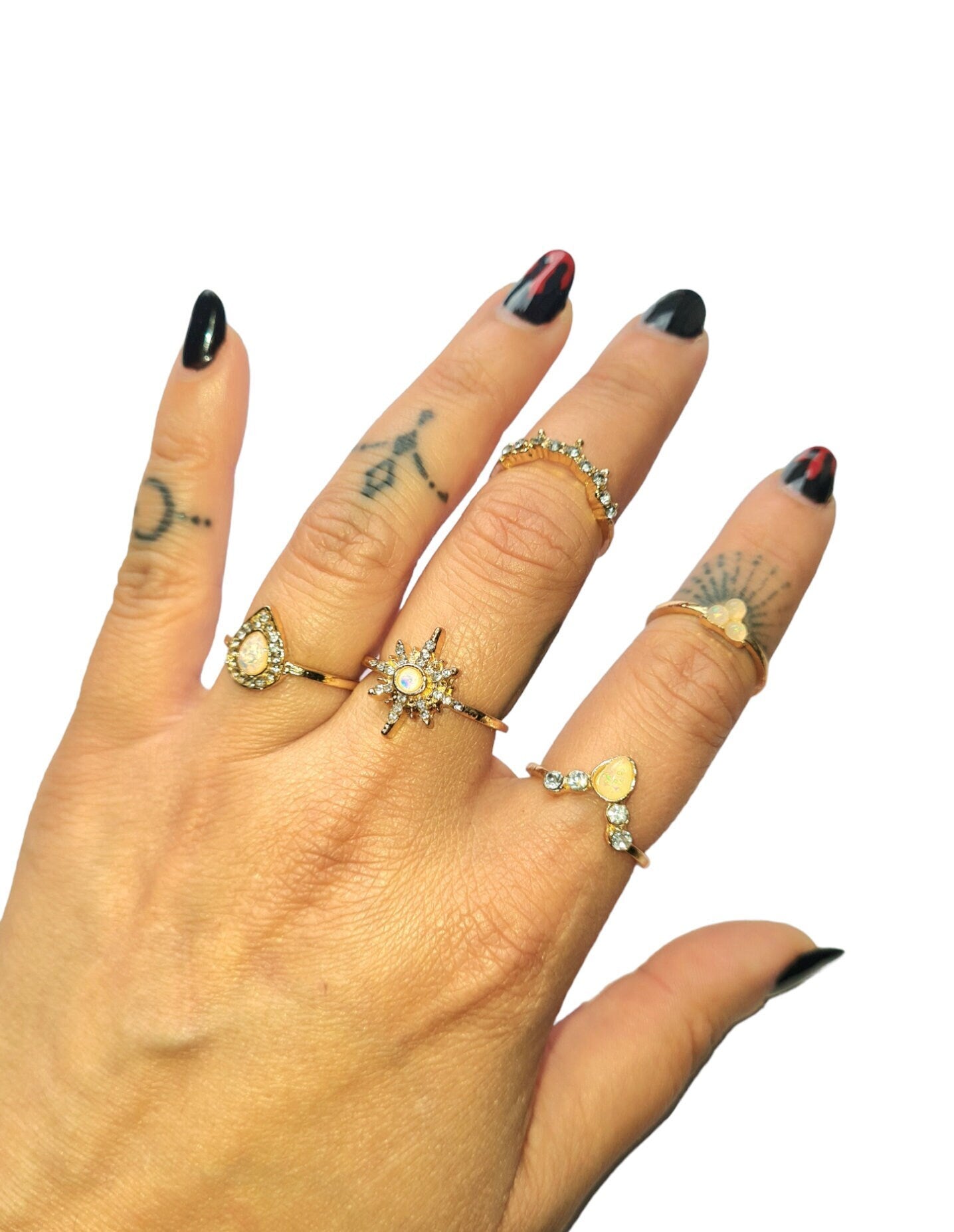 A person is wearing a gold-plated ring set with multiple rings on their fingers, featuring different designs such as a teardrop shape and a star opal. The rings have crystal and opal stones, giving a boho and mystical appearance.
