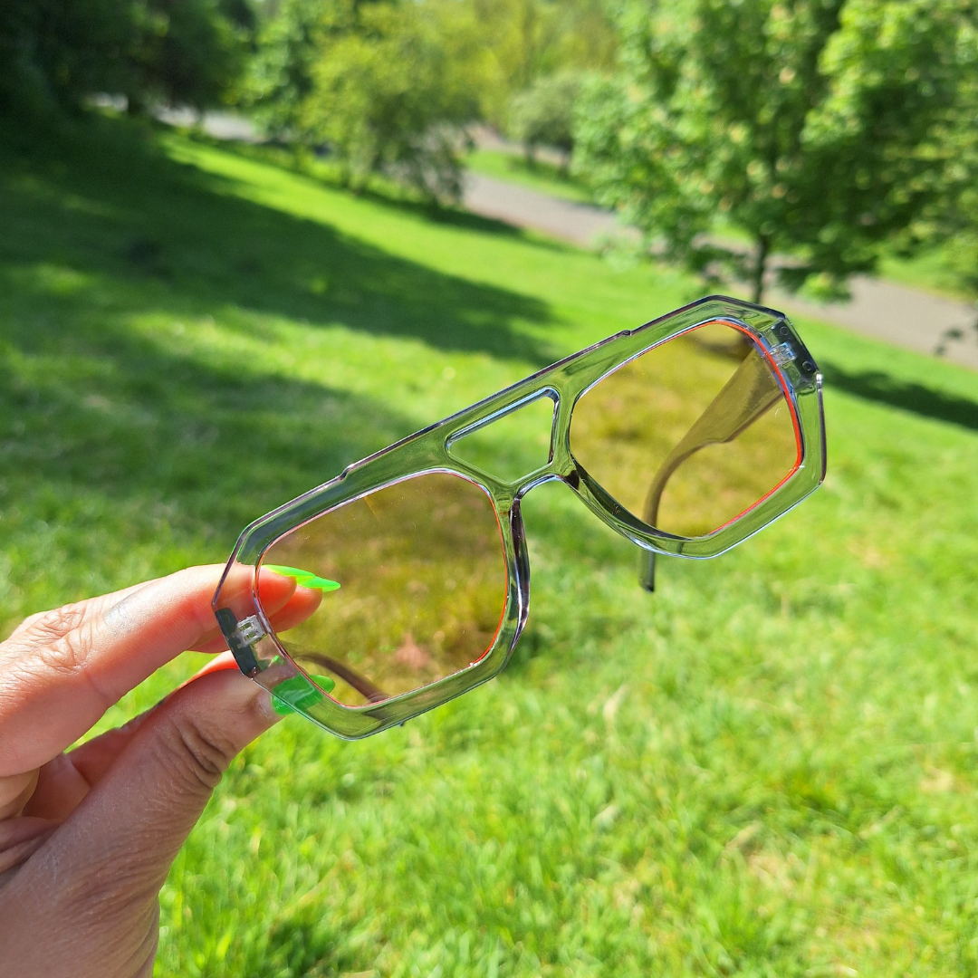Clear Pink Lensed Retro Sunnies being held up by a hand in the park.