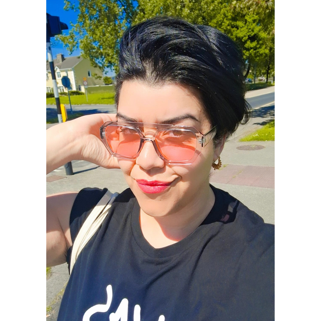 Clear Pink Lensed Retro Sunnies on a pretty girl smiling in the sunshine. Also wearing Arabian creole hoop earrings in gold.
