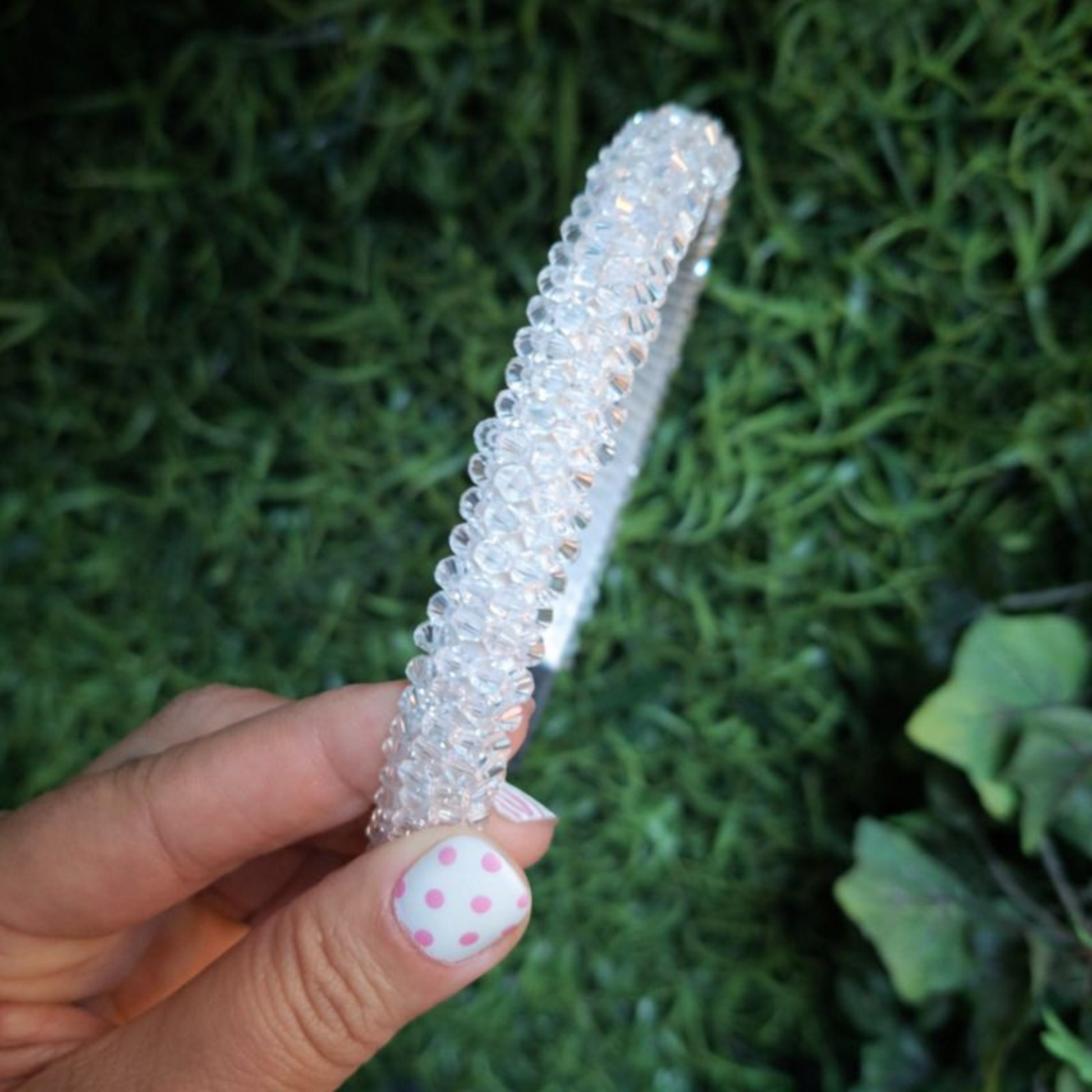 Clear rhinestone beaded headband held by a hand on a white background.