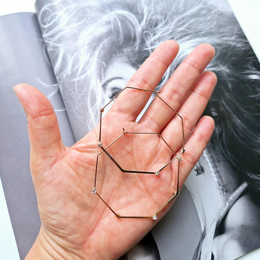 Upcycled octagonal gold plated hoops held in a hand over a magazine.