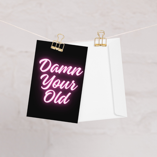 Neon sign with 'Damn Your Old' text on a black background, clipped to a white sheet of paper.