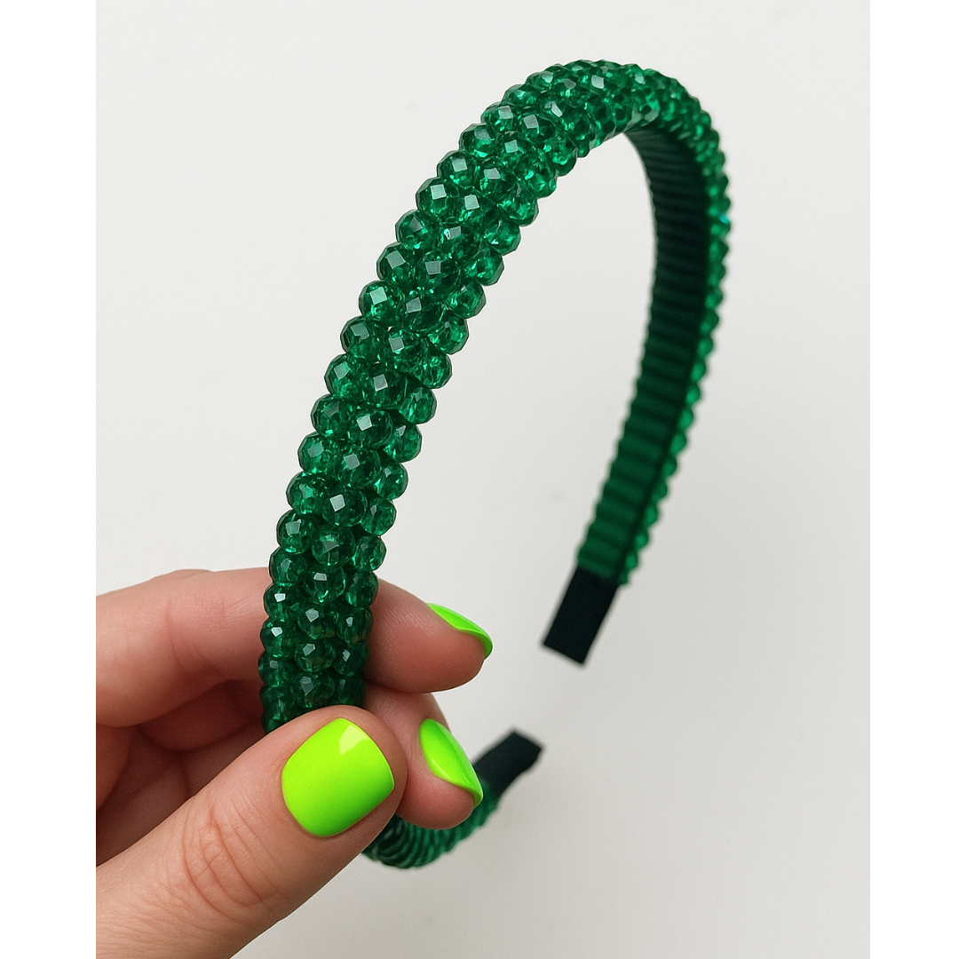 Emerald Green rhinestone beaded headband held by a hand with neon green nail polish on a white background.