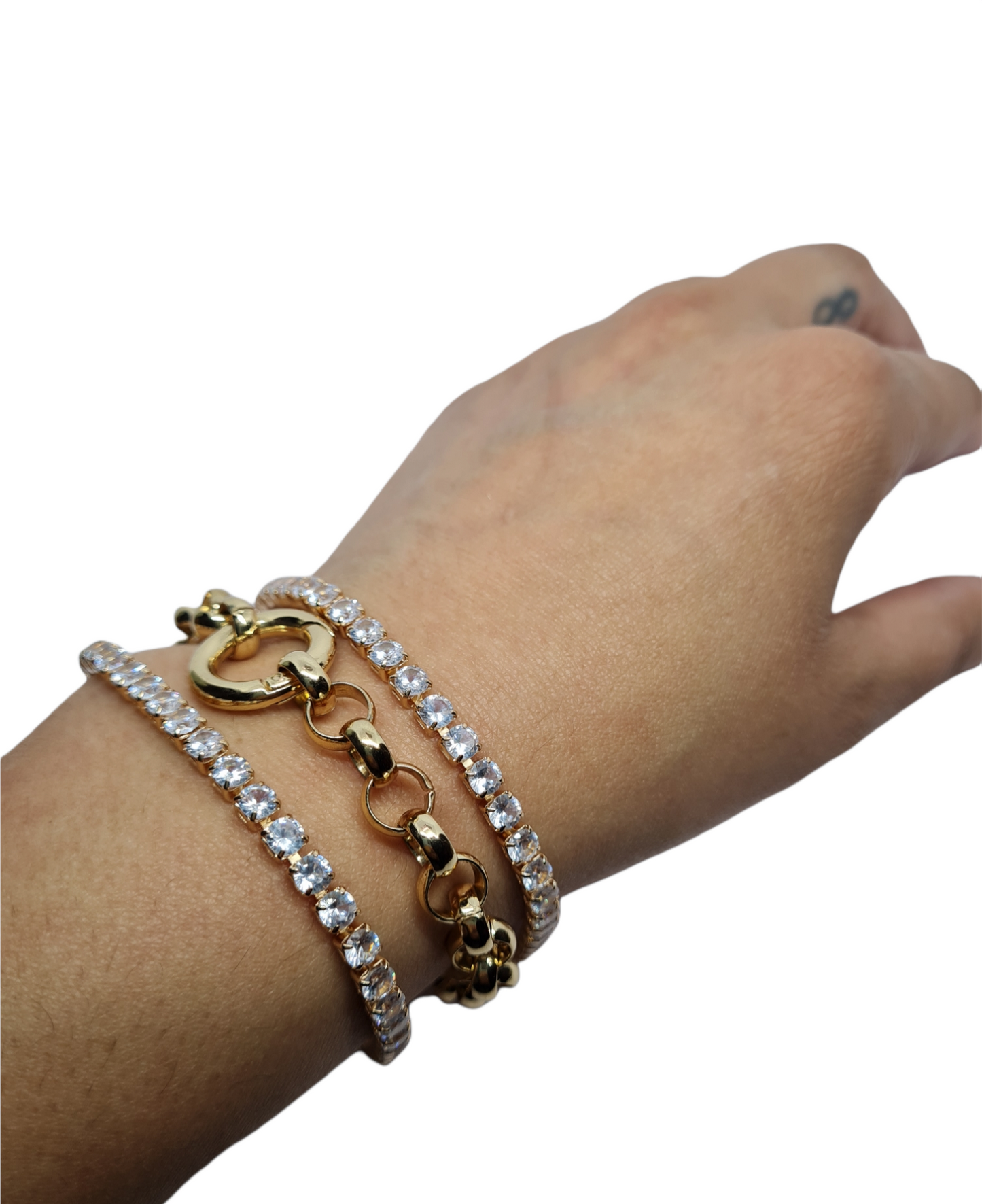 A gold-plated tennis bracelet with sparkling stones and a chunky link bracelet on a arm, laid out on a plain surface.