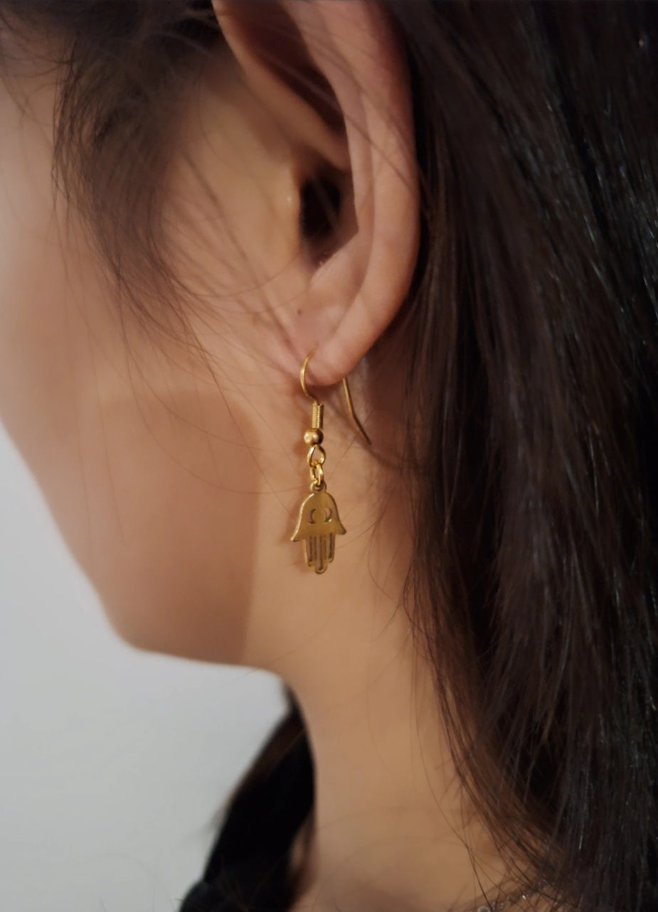 Gold Plated Fatima Hand Earrings featuring the shape of the Fatima hand symbol, displayed on a woman's ear.