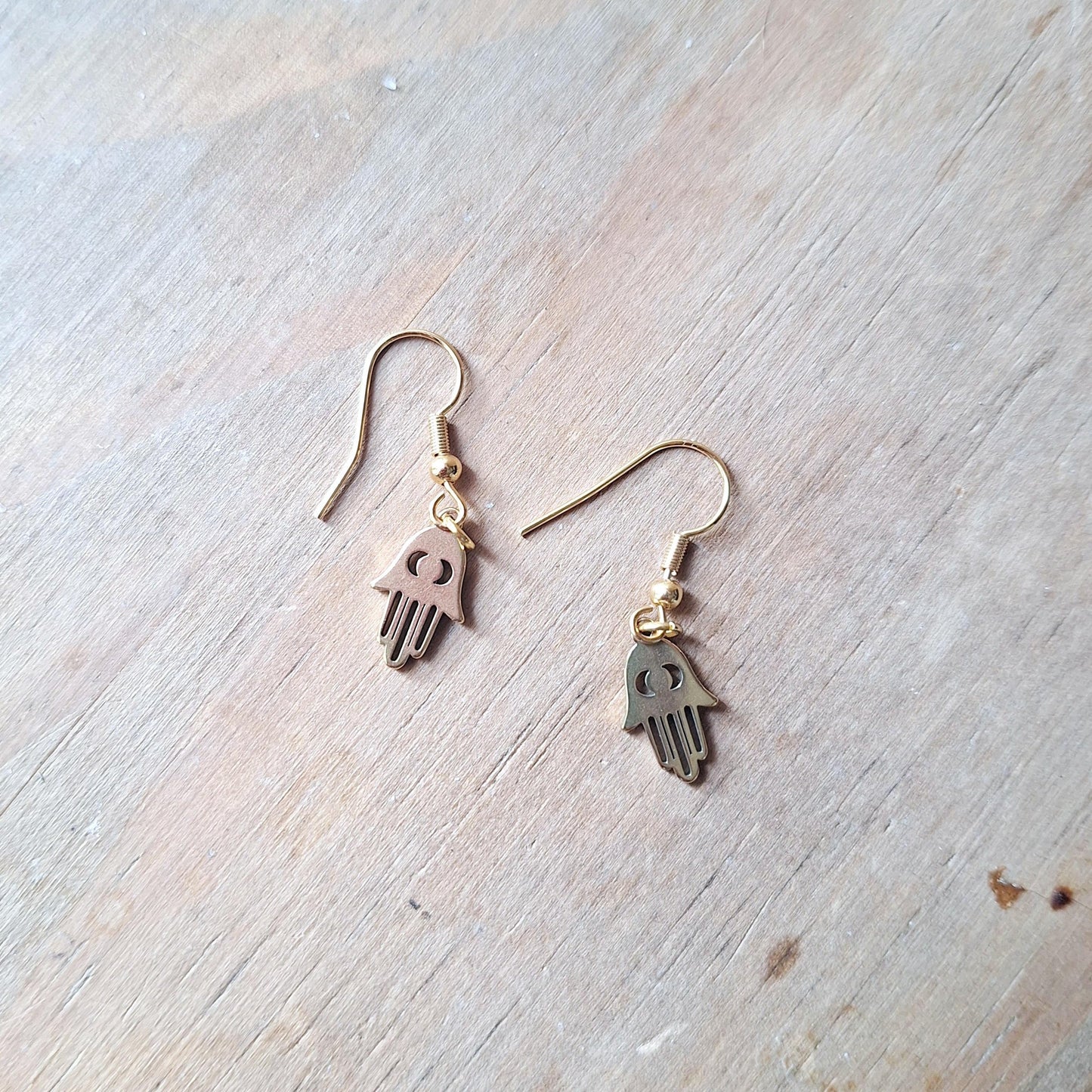 Gold Plated Fatima Hand Earrings featuring the shape of the Fatima hand symbol, displayed on a wooden surface.