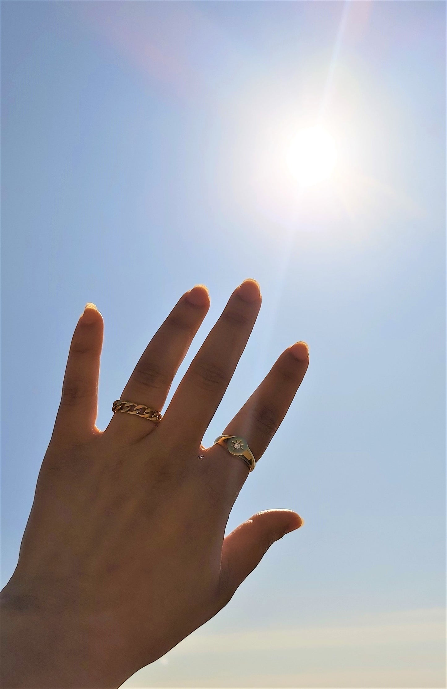 A hand displaying 2 gold plated rings in the sun.