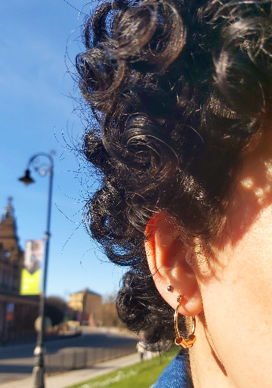 A pair of upcycled gold plated beaded hoop earrings on a girl with curly hair.