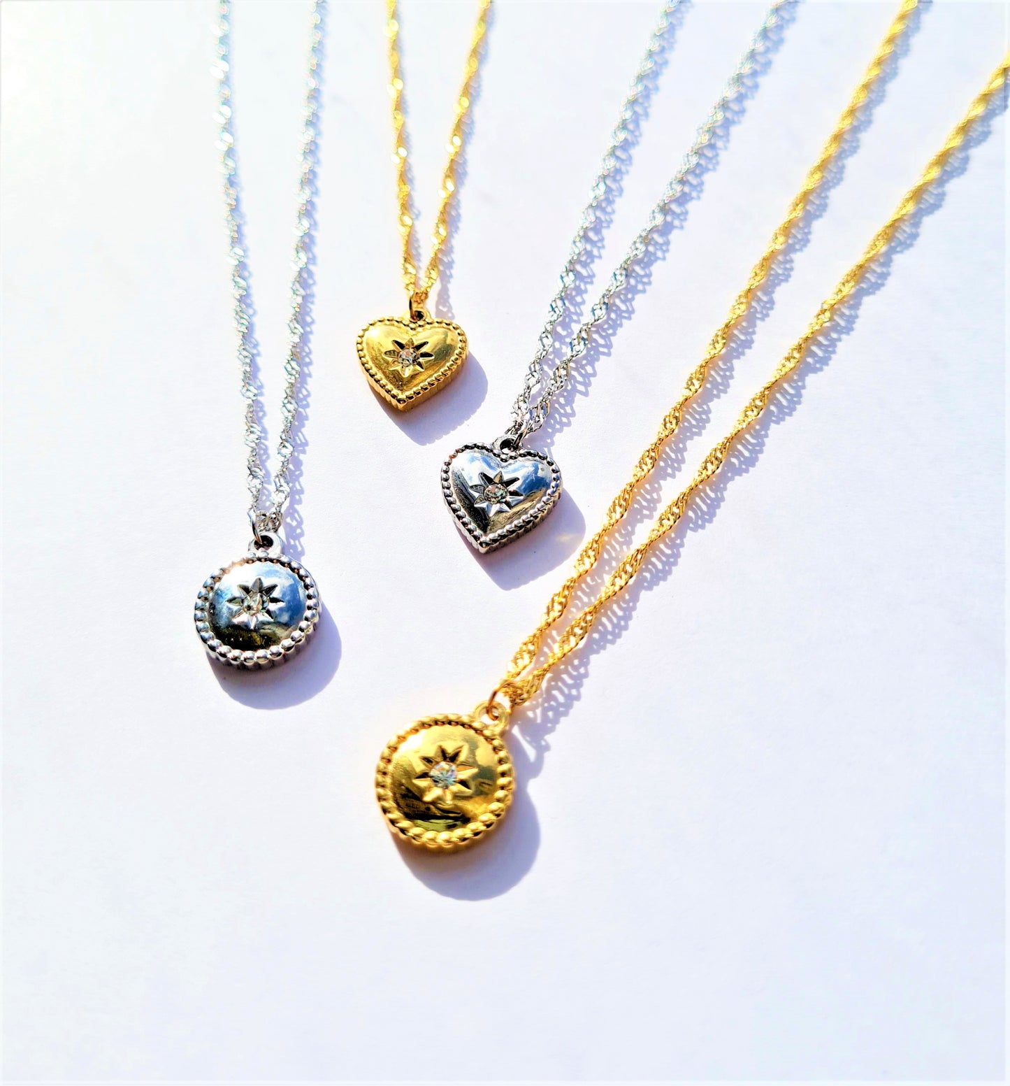 Four silver and gold plated stainless steel circle heart necklaces with one featuring a star pendant and the other a round crystal pendant.