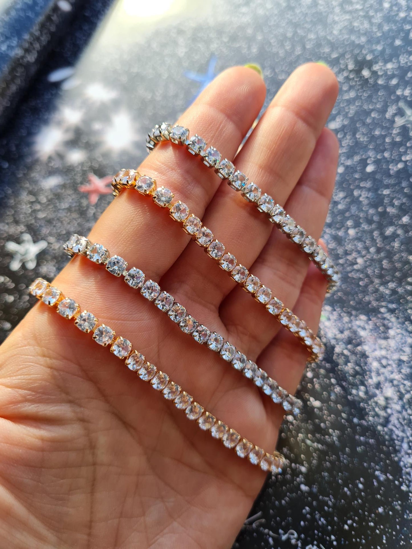 Silver and gold-plated tennis bracelets with sparkling stones, laid out on a plain surface.