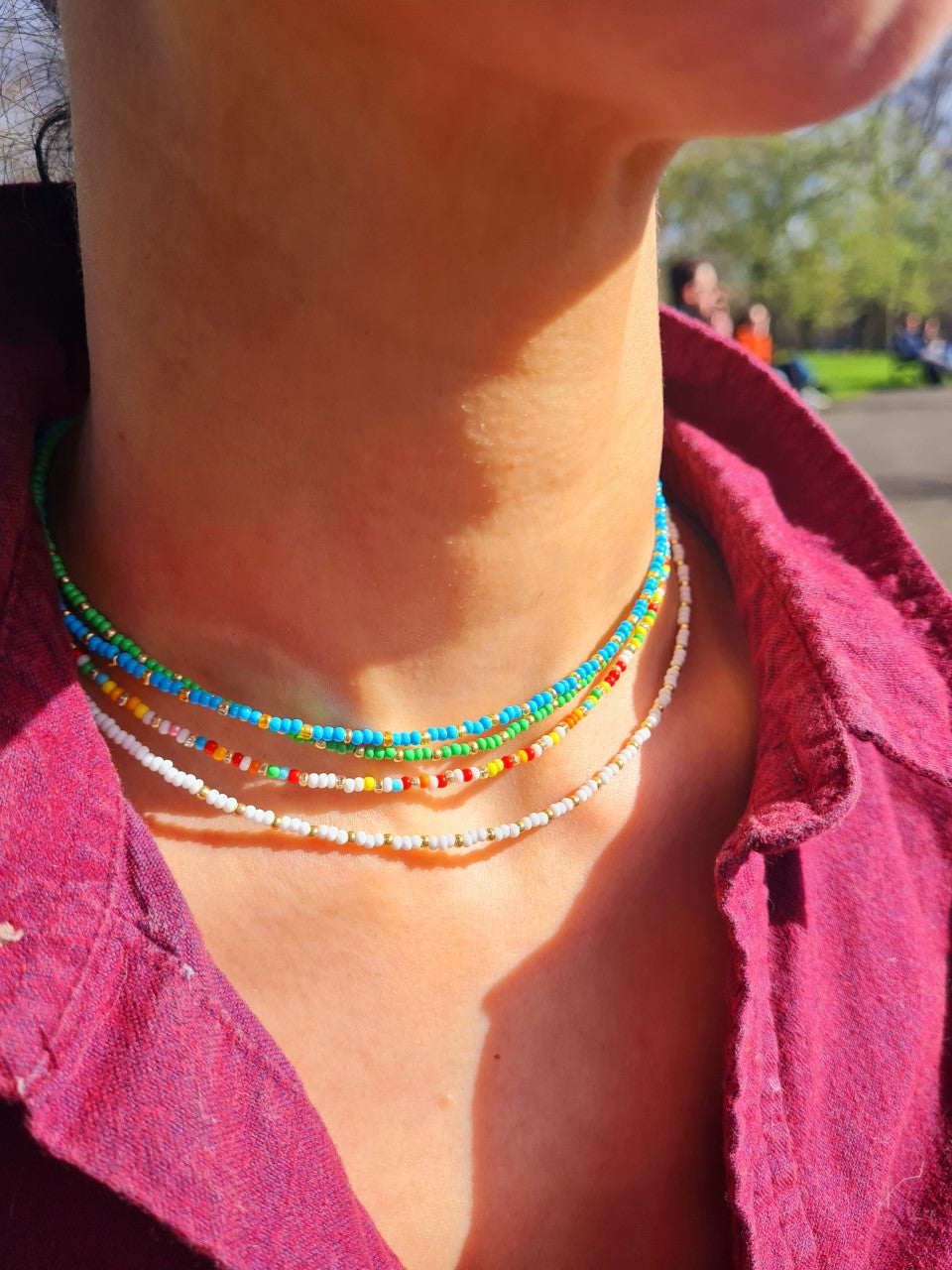 4 handmade multi-coloured beaded necklaces with a gold plated chain and a crystal miyuki bead design, on the neck of a pretty girl in the sun.
