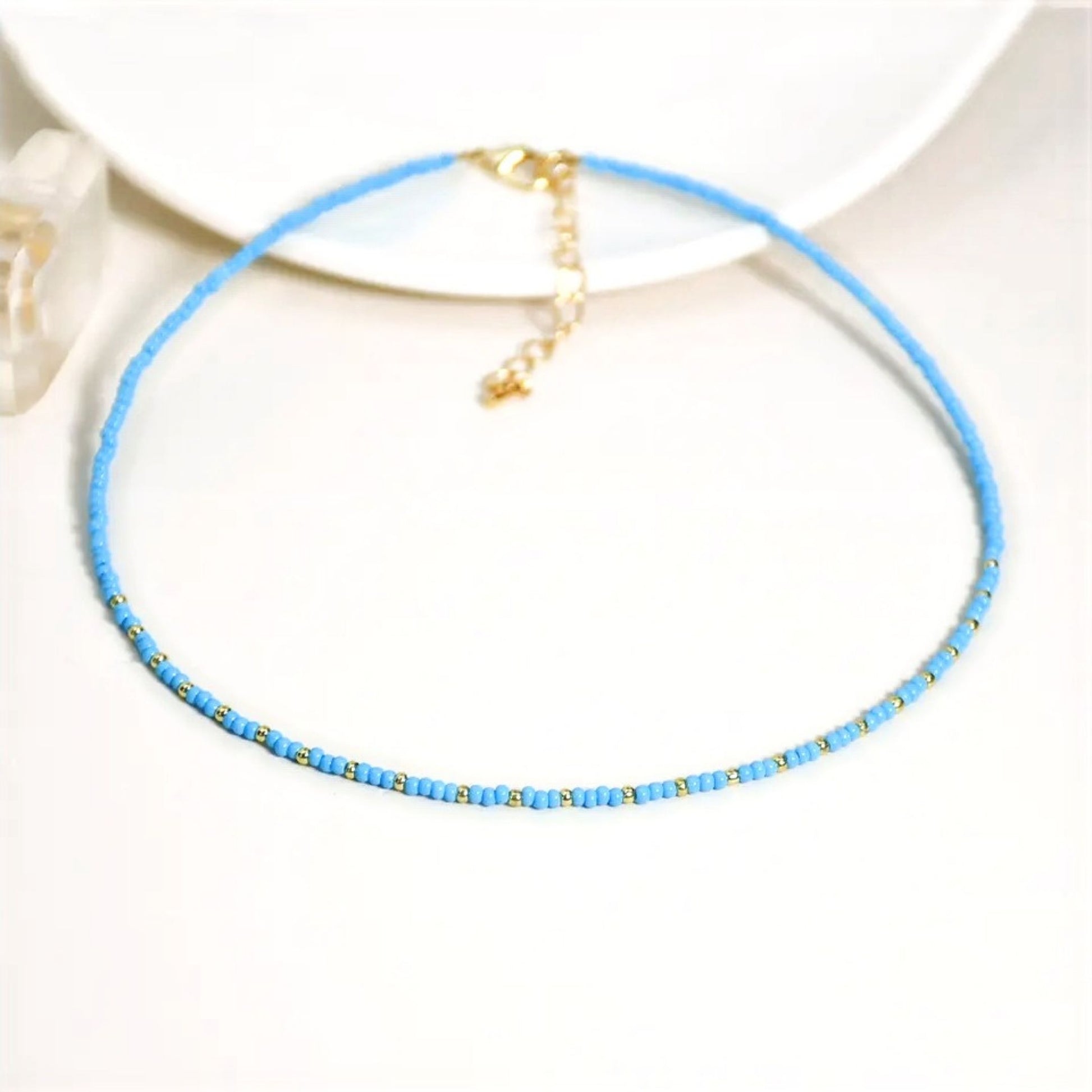 A pastel  blue multi-coloured beaded necklace with a gold plated chain and  miyuki bead design, displayed on a white background.