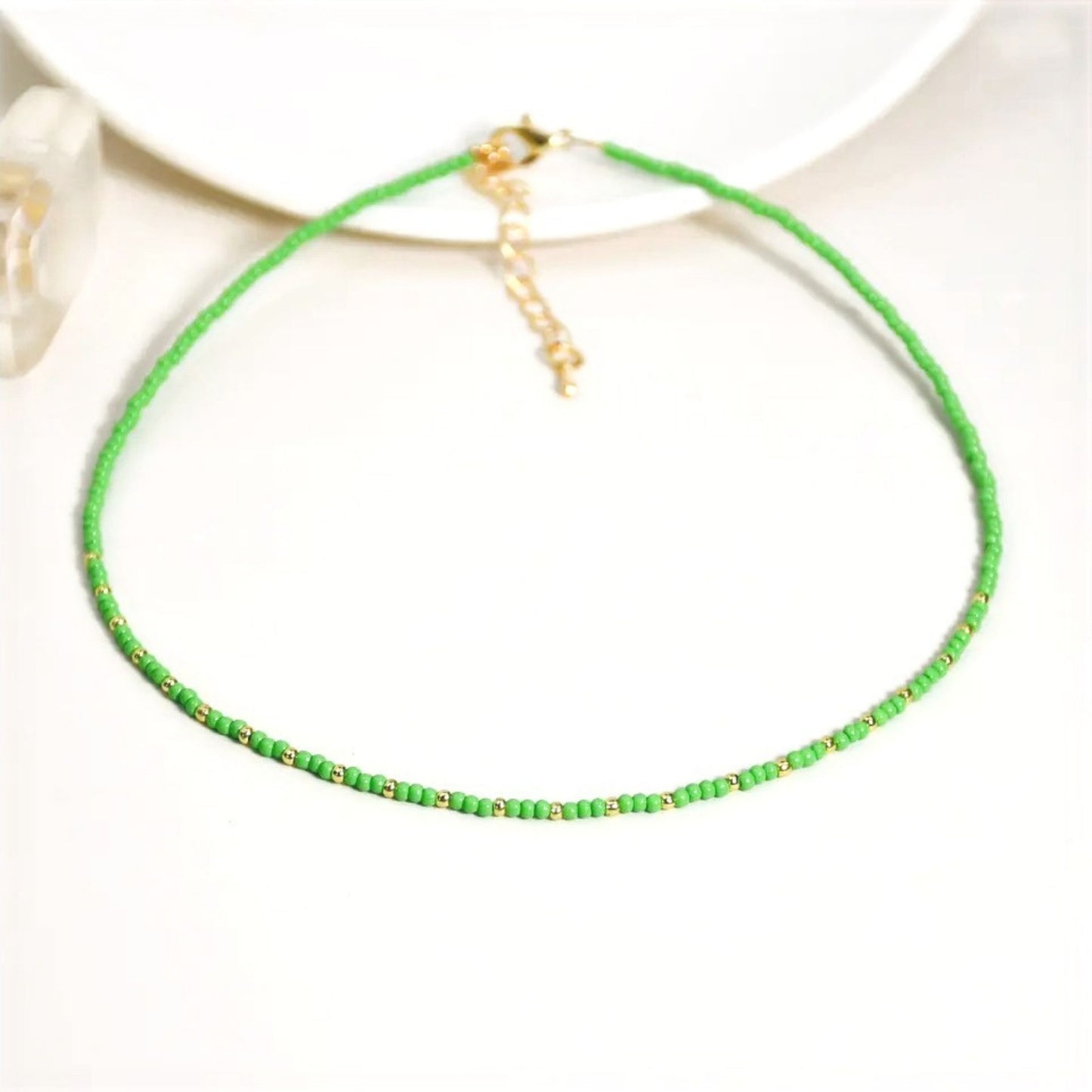 A green multi-coloured beaded necklace with a gold plated chain and  miyuki bead design, displayed on a white background.