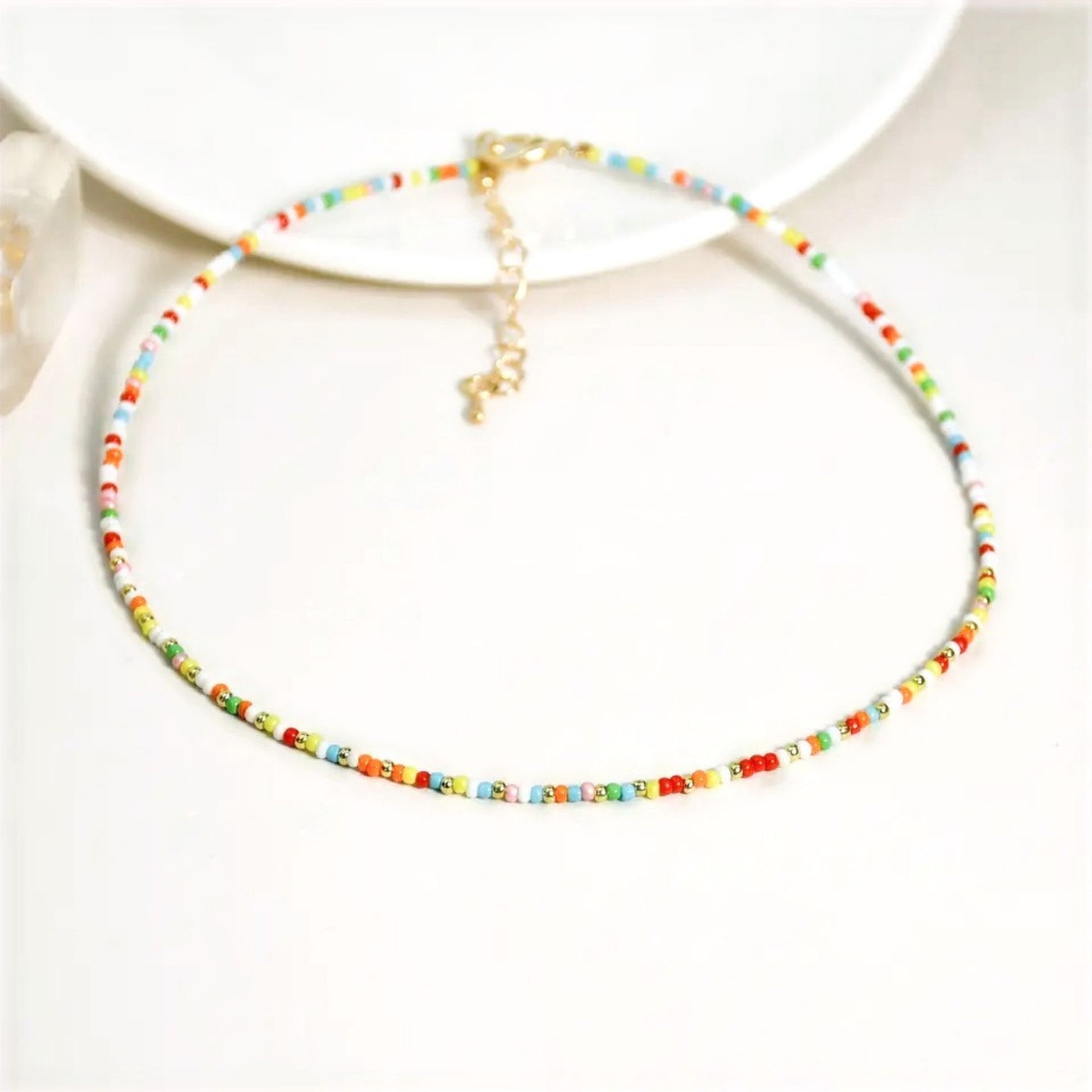 A multi-coloured beaded necklace with a gold plated chain and a crystal miyuki bead design, displayed on a white background.
