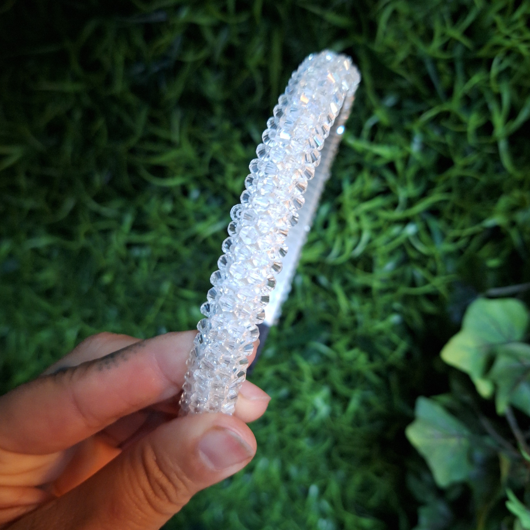 Clear rhinestone beaded hair band accessory held by a hand against a green, leafy background