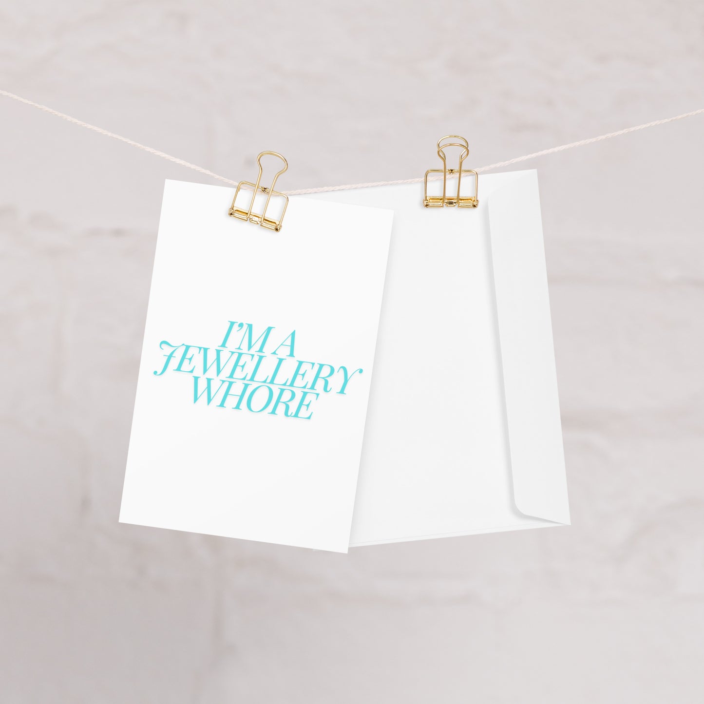 Jewellery Whore Greeting Card hanging on a washing line with two gold clips.