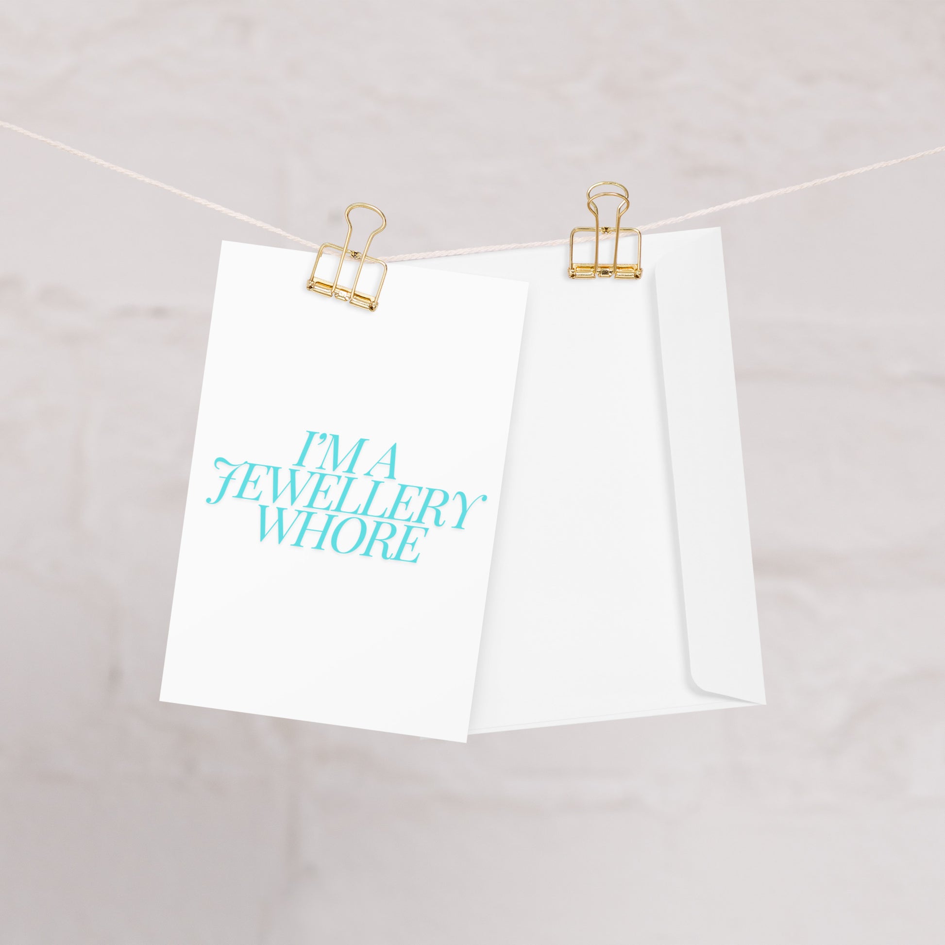 Jewellery Whore Greeting Card hanging on a washing line with two gold clips.