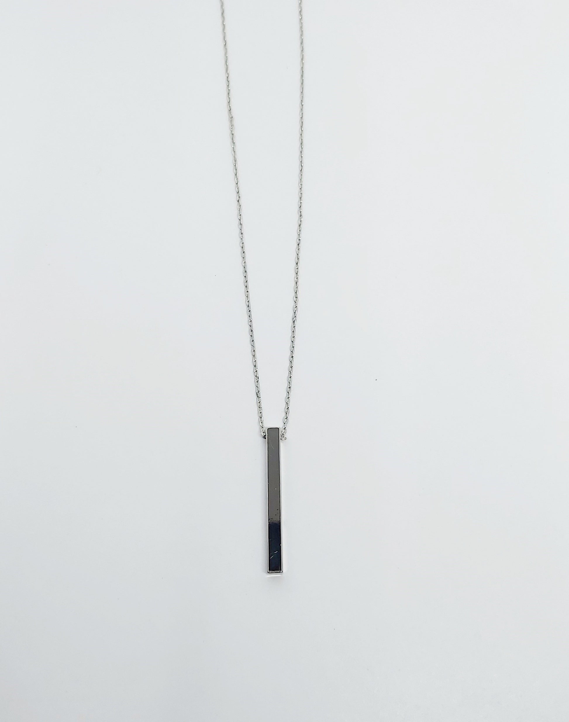 A silver-plated brass necklace with a geometric pendant in the shape of a circle and a bar, displayed on a white background.