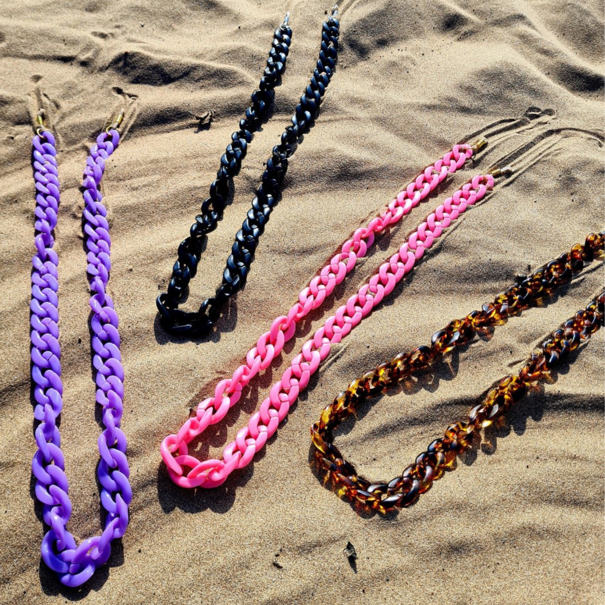 Colourful chunky sunglasses chains in various colours on the sand on the beach.