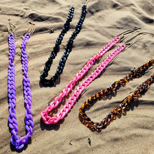 Colourful chunky sunglasses chains in various colours on the sand on the beach.