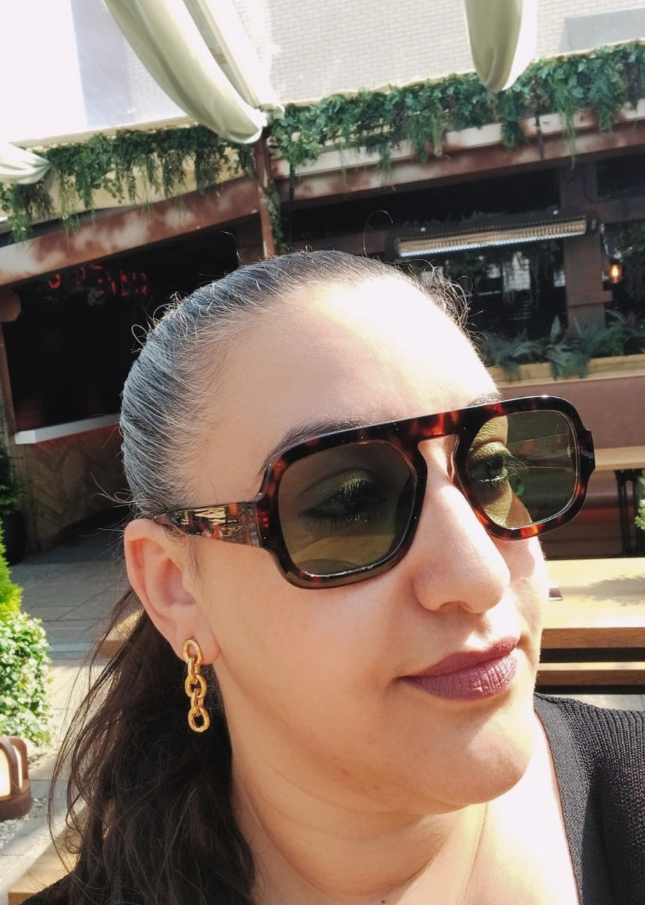 Woman wearing sunglasses with No Tarnish Gold Biker Chain Earrings on in the sun in a bar in Glasgow.