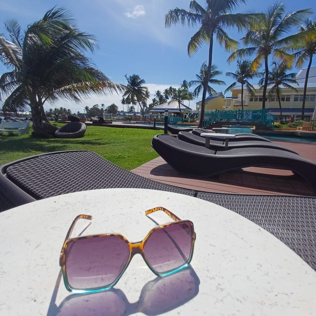 Oversized Glam 70s Leopard and Turquoise Sunglasses on a white table overlooking the beach and palm trees.